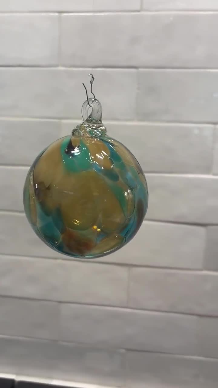Adorno navideño de vidrio soplado a mano, en beige, marrón, verde azulado y crema. Hecho a mano en las montañas Ozark. Nuevo color para 2026. Nombre del color: Adoquín. video poster